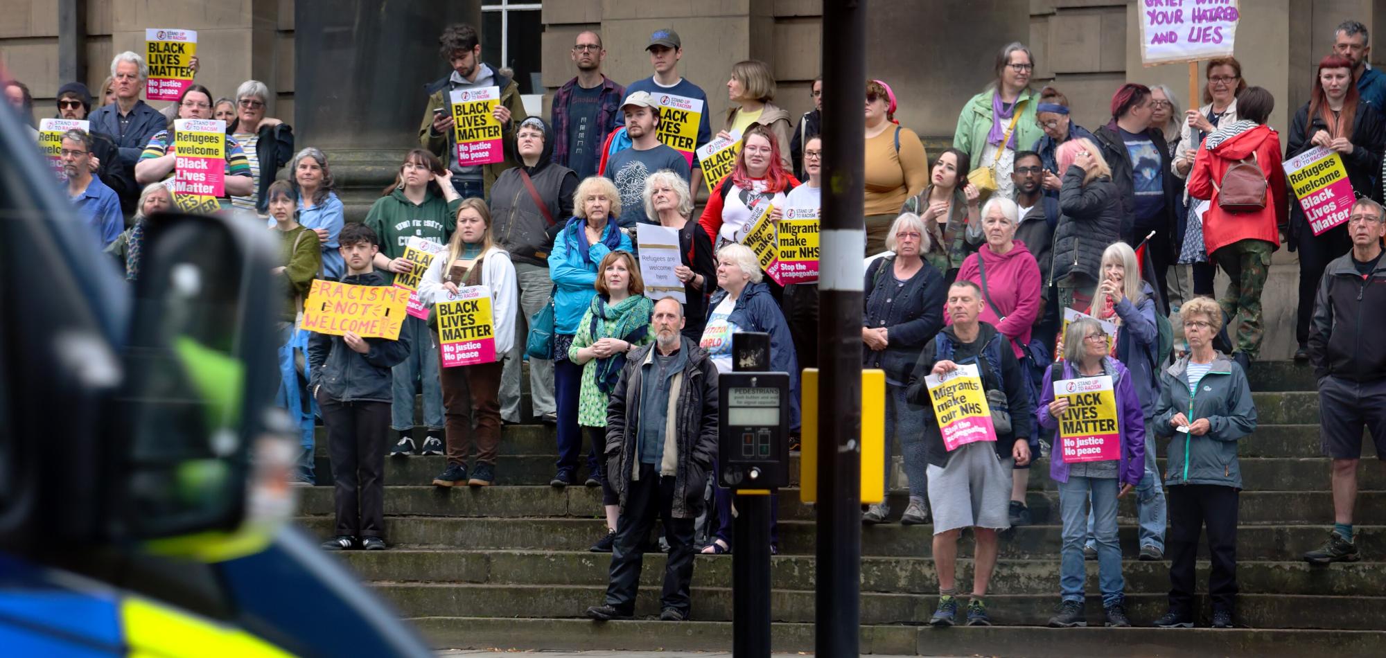 A crowd of people holding stand up to racism placards