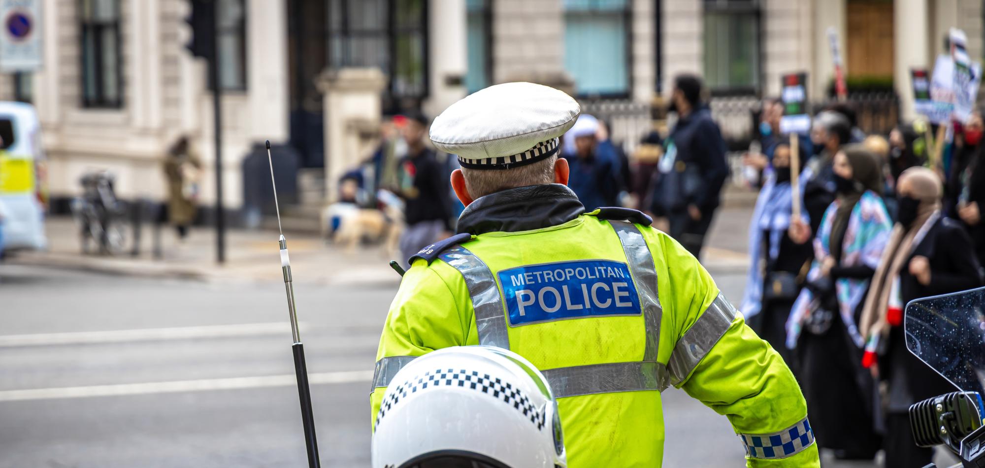 A metropolitan police officer looking on at protestors walking by.