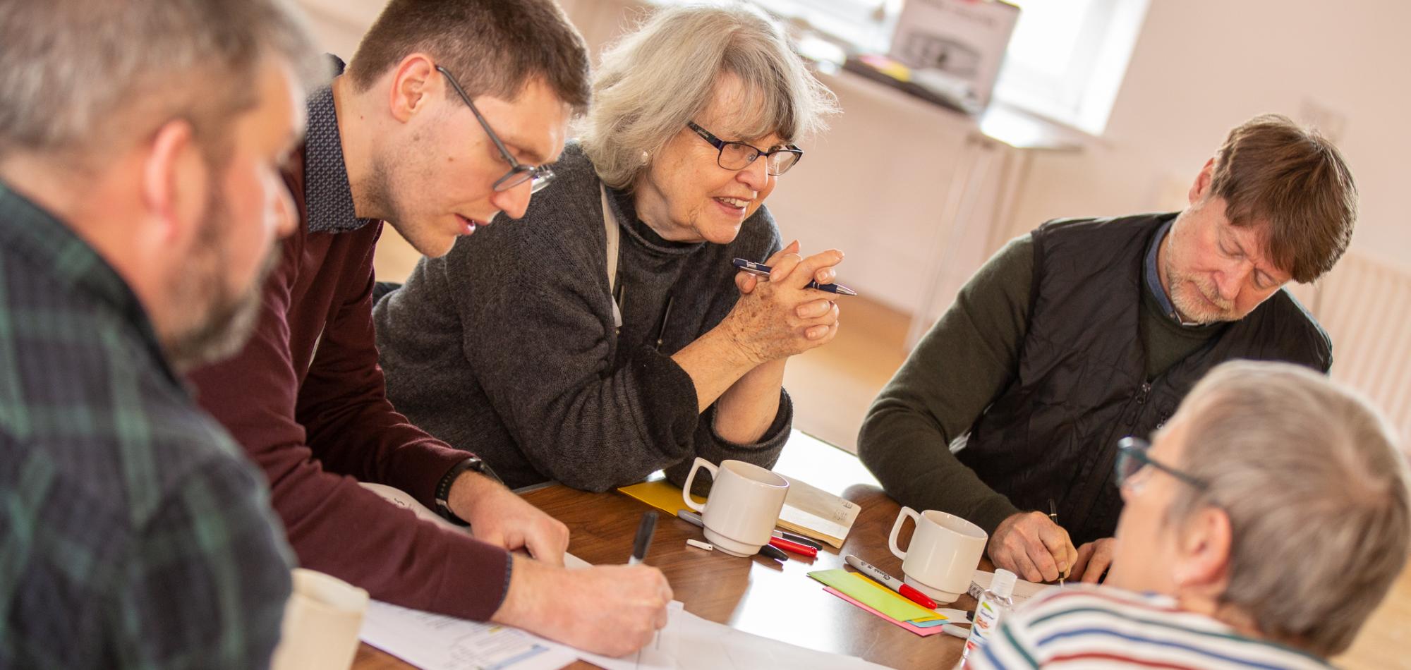 Group of people discussing topics around a table, writing. 