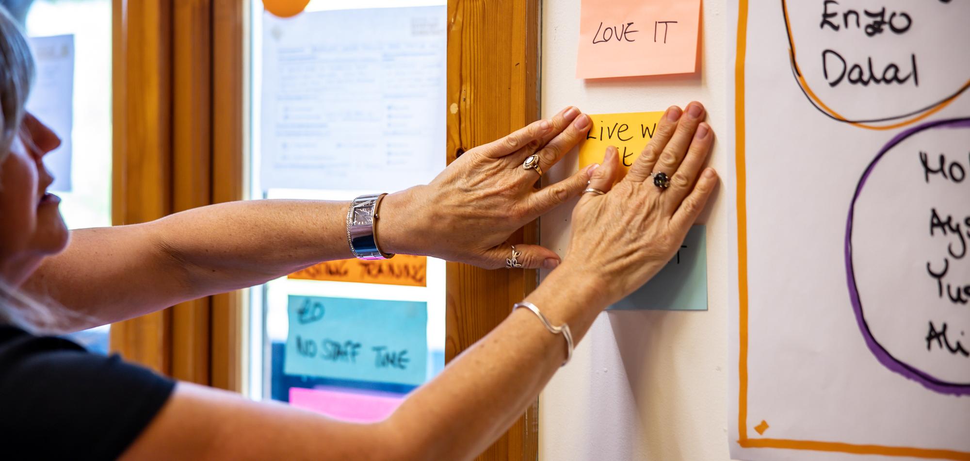 A person sticking a sticky note to a wall
