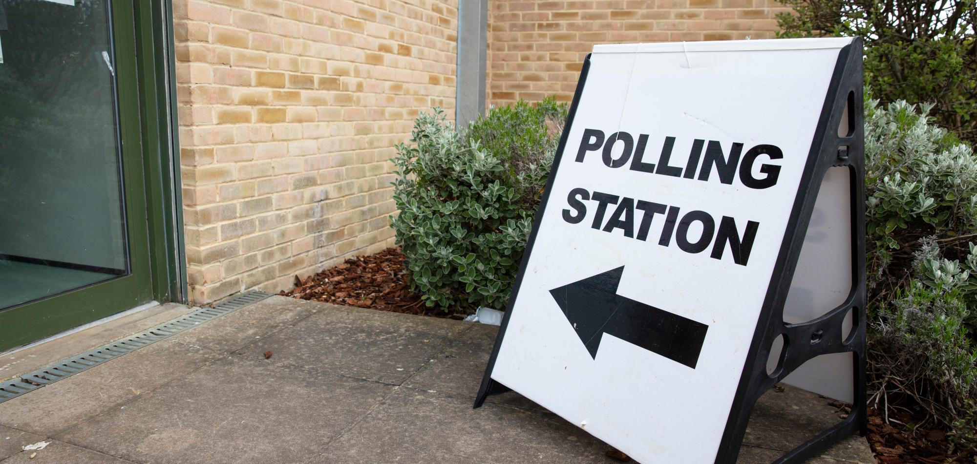 A white sign outside of a building that reads 'polling station'