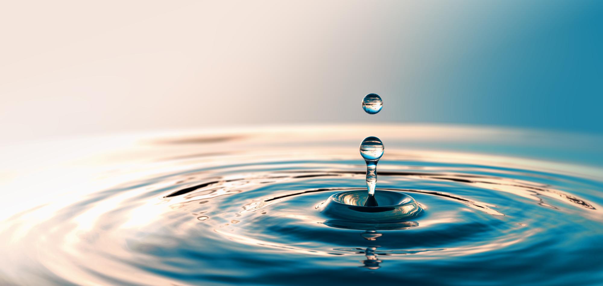A droplet of water hitting a larger body of water, creating a ripple
