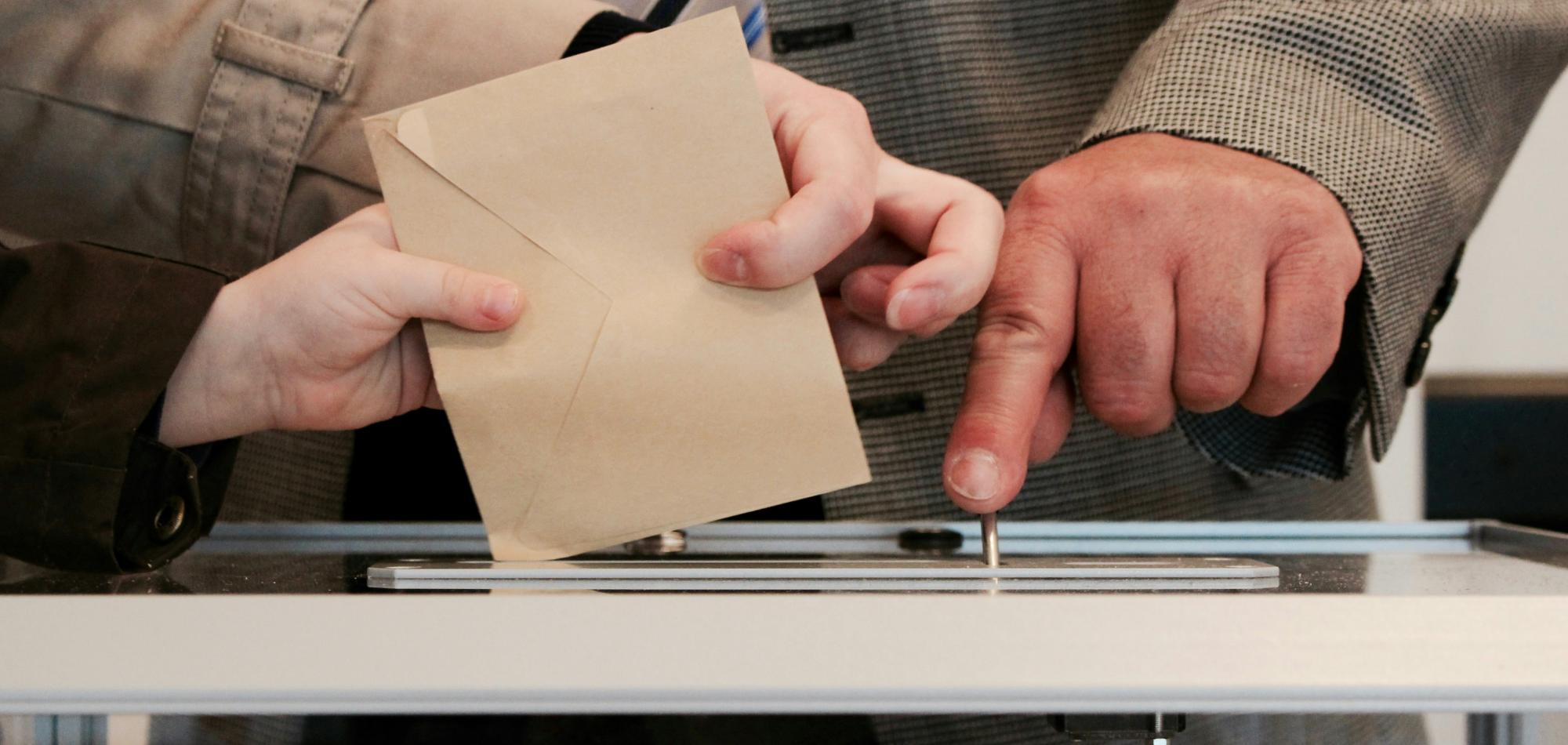 People putting an envelope in a box to signify voting. 