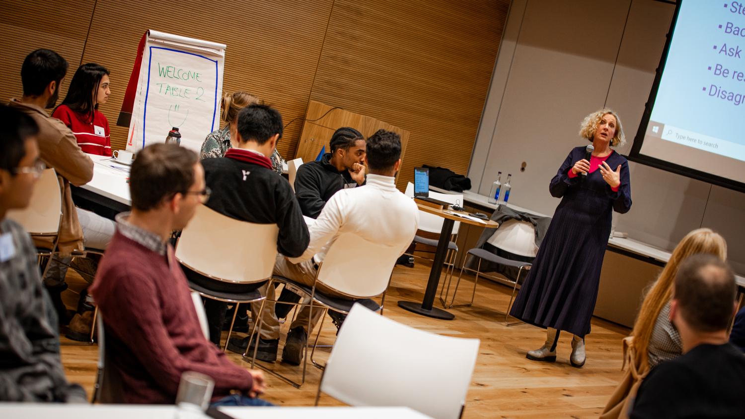 People sat around tables listening to a presenter at the front of the room