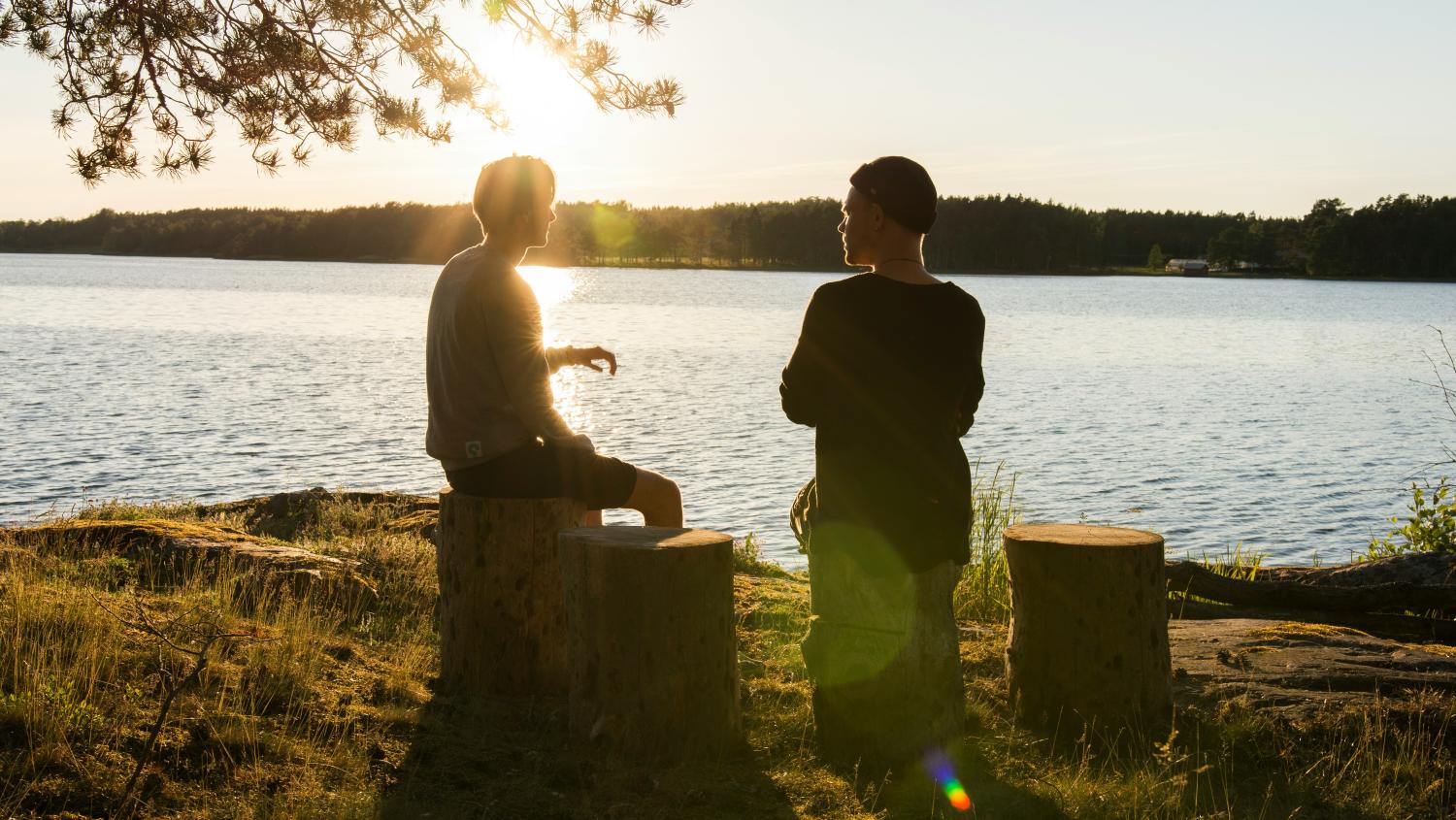 Two people having a conversation whilst sitting on logs by the riverside